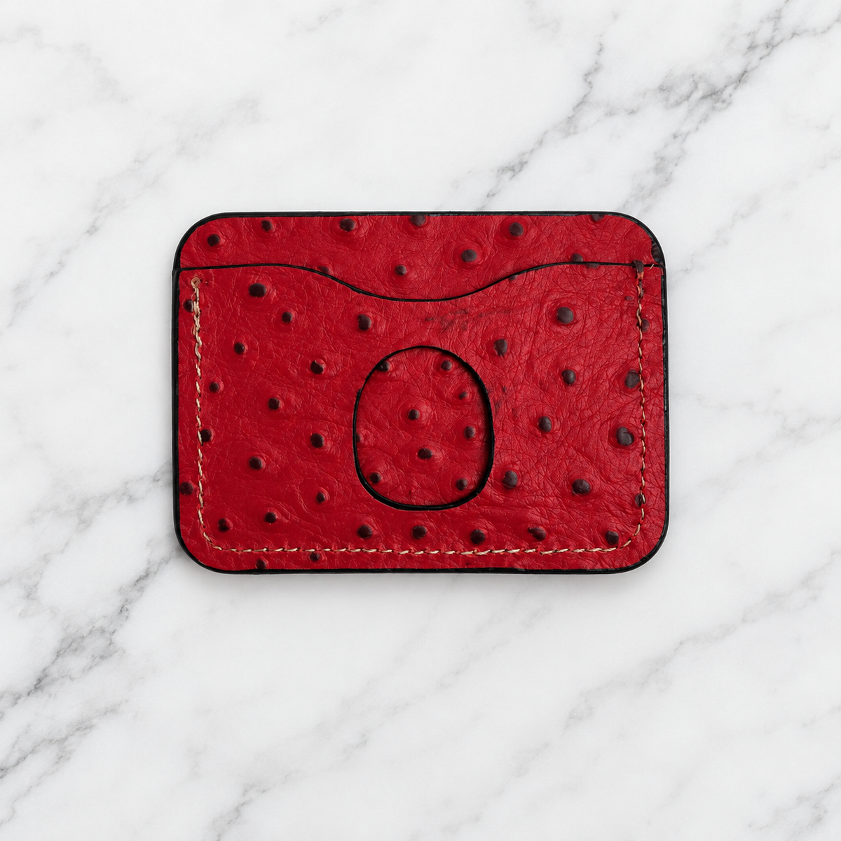 Ruby red textured leather cardholder back with thumb cutout on marble