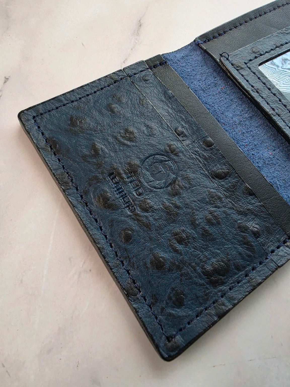 Midnight blue textured leather ID wallet — detail view on marble