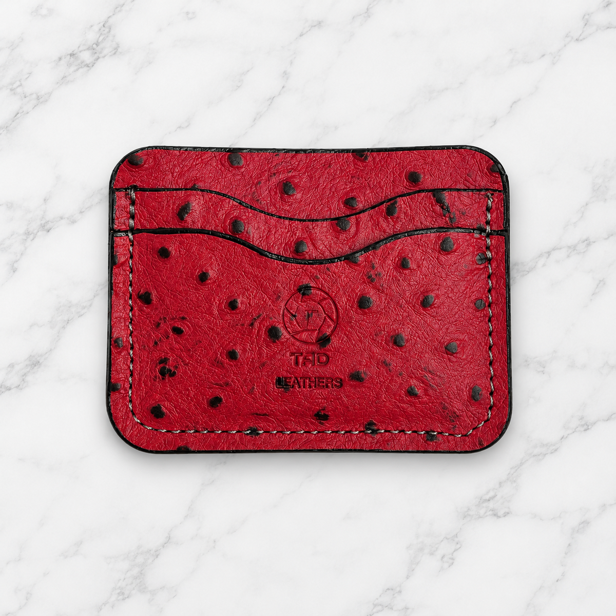 Ruby red textured leather cardholder front with Tad Leathers stamp on marble
