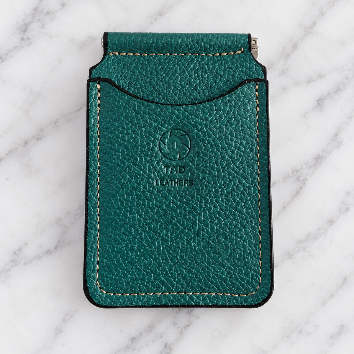 Teal pebbled leather money clip wallet with tan stitching on marble
